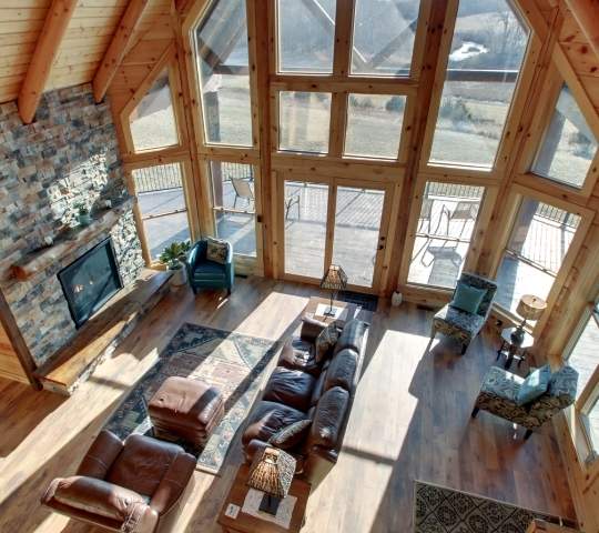 photo take from loft area of a great room of a log home with soaring two story windows, log walls and flooring with exposed log support beams.