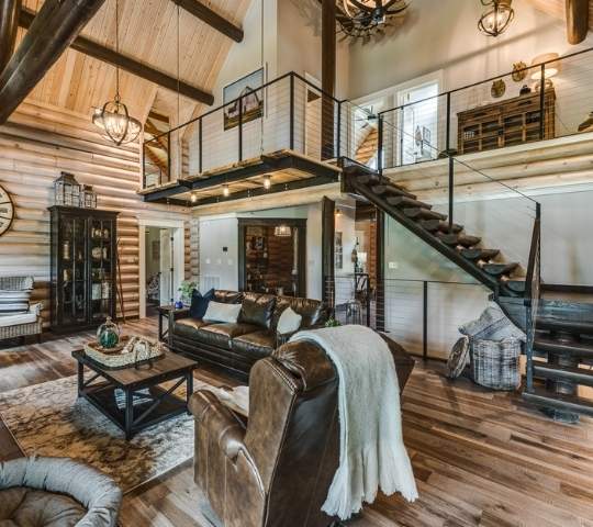 photo of great room take from lower level showing open loft, above an open staircase. The ceiling and walls are wood with matching wood hardwood flooring.